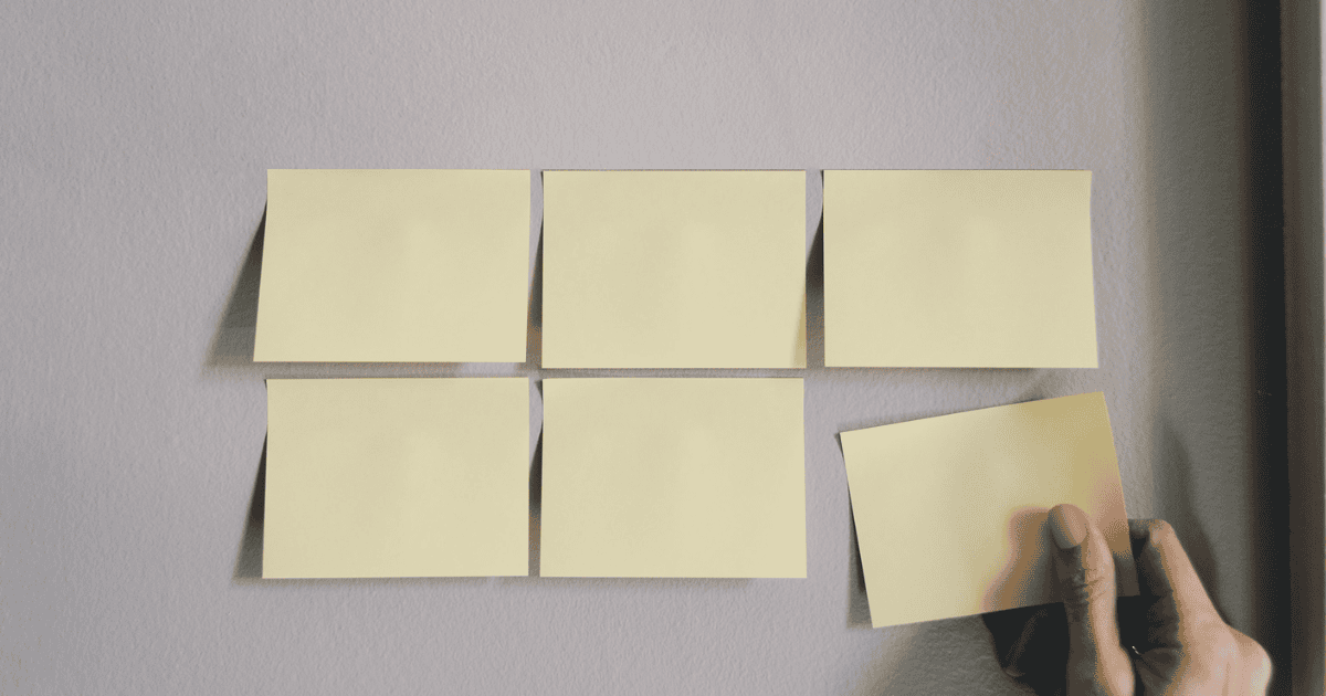 A hand adding a blank sticky note to a group on a wall