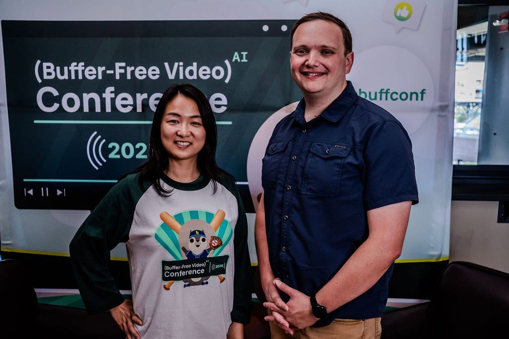 Buffer-Free Video AI カンファレンスのバナーの前で写真に収まる 2 人の参加者。