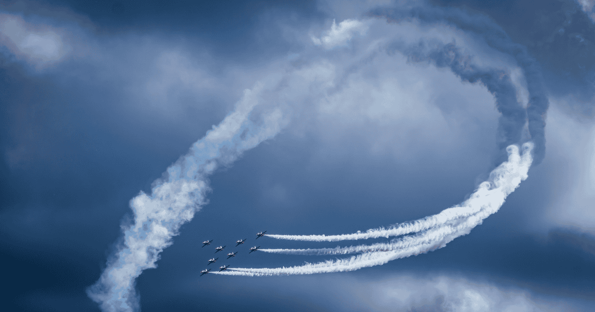 Aircraft leaving curved white trails in a cloudy sky